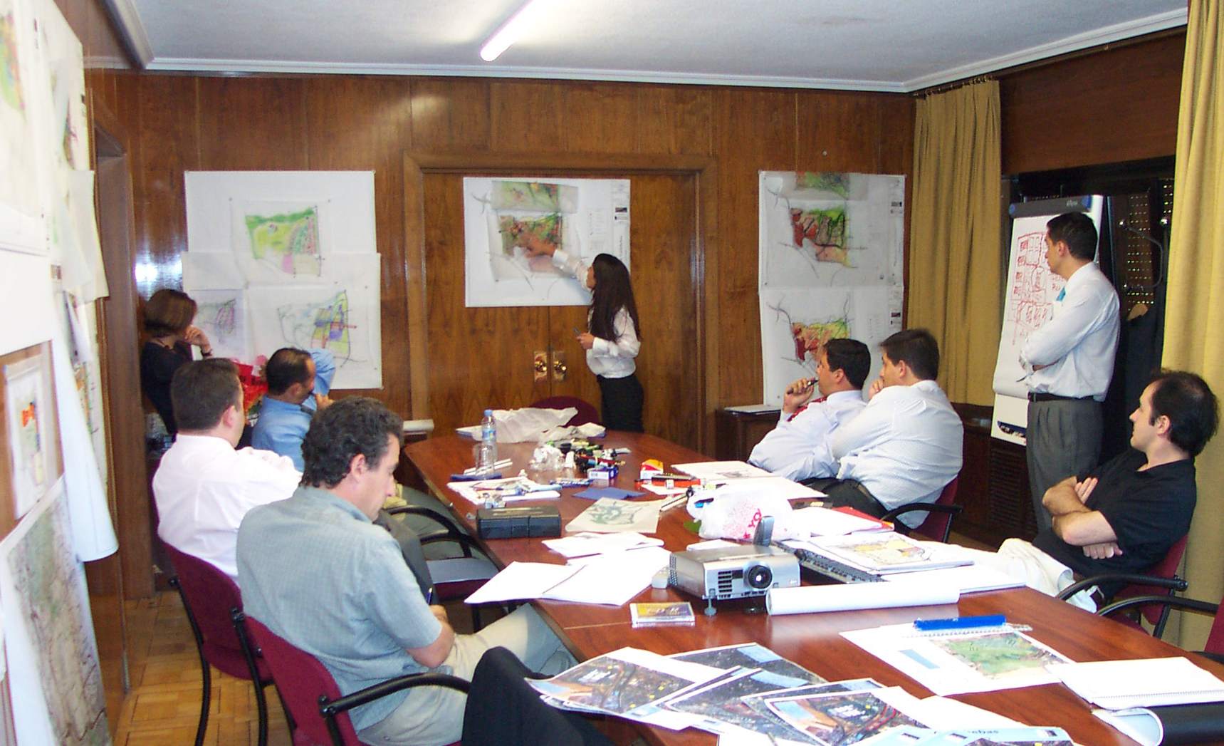 A group of people sitting around tables in front of a woman.