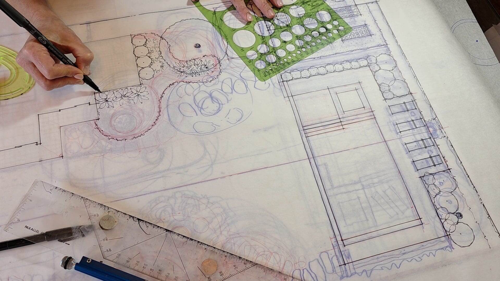A person is working on some drawings with a green ruler.