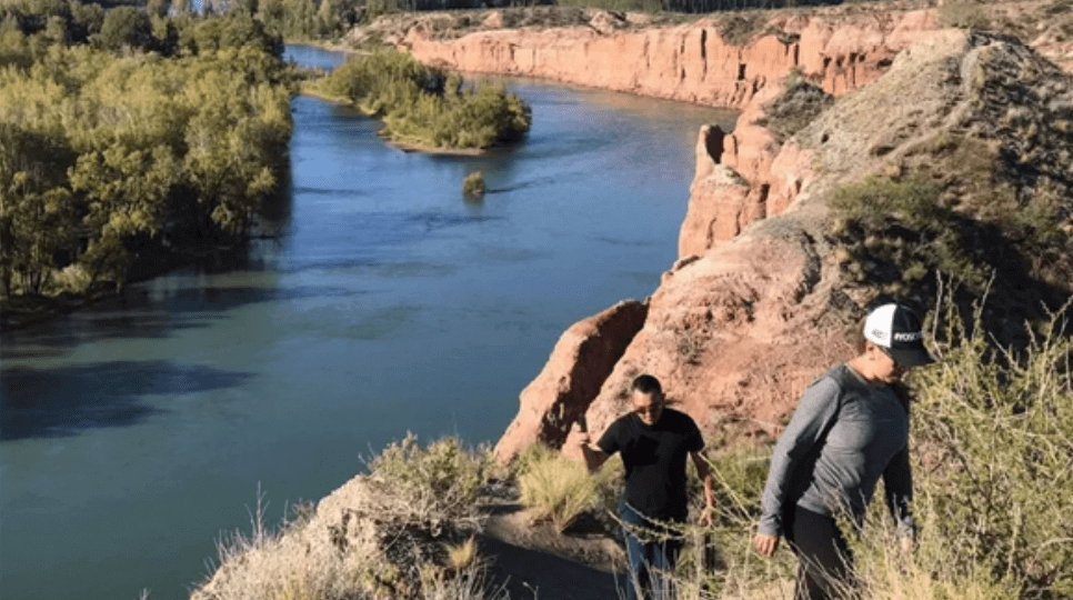 Two people standing on a cliff overlooking the water.
