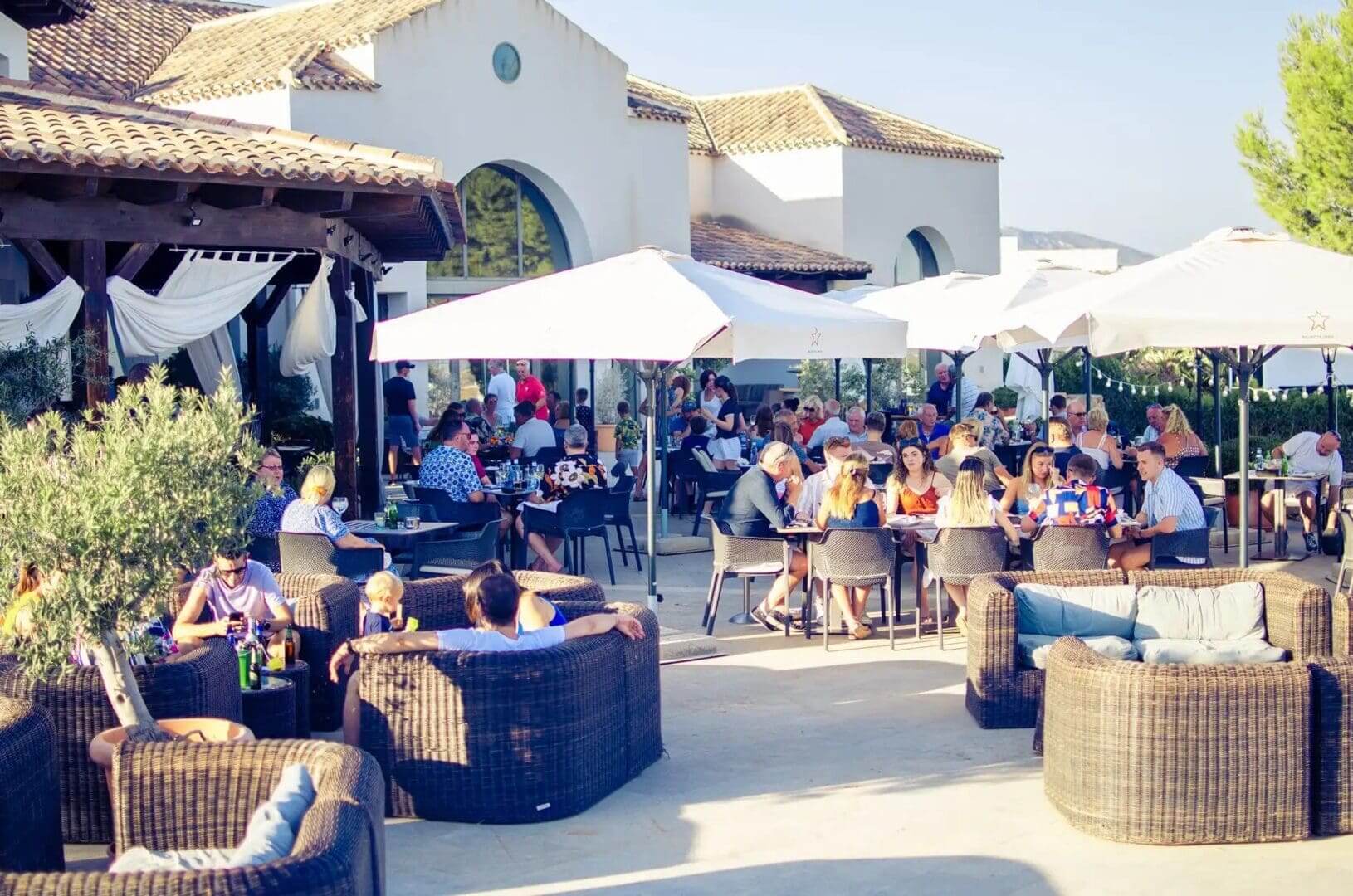 A crowd of people sitting at tables under umbrellas.